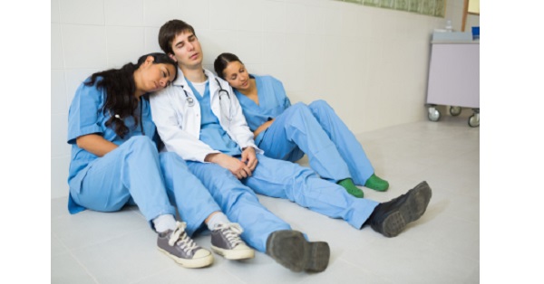 Nurses and doctor sleeping while sitting on the floor of a hospital hallway